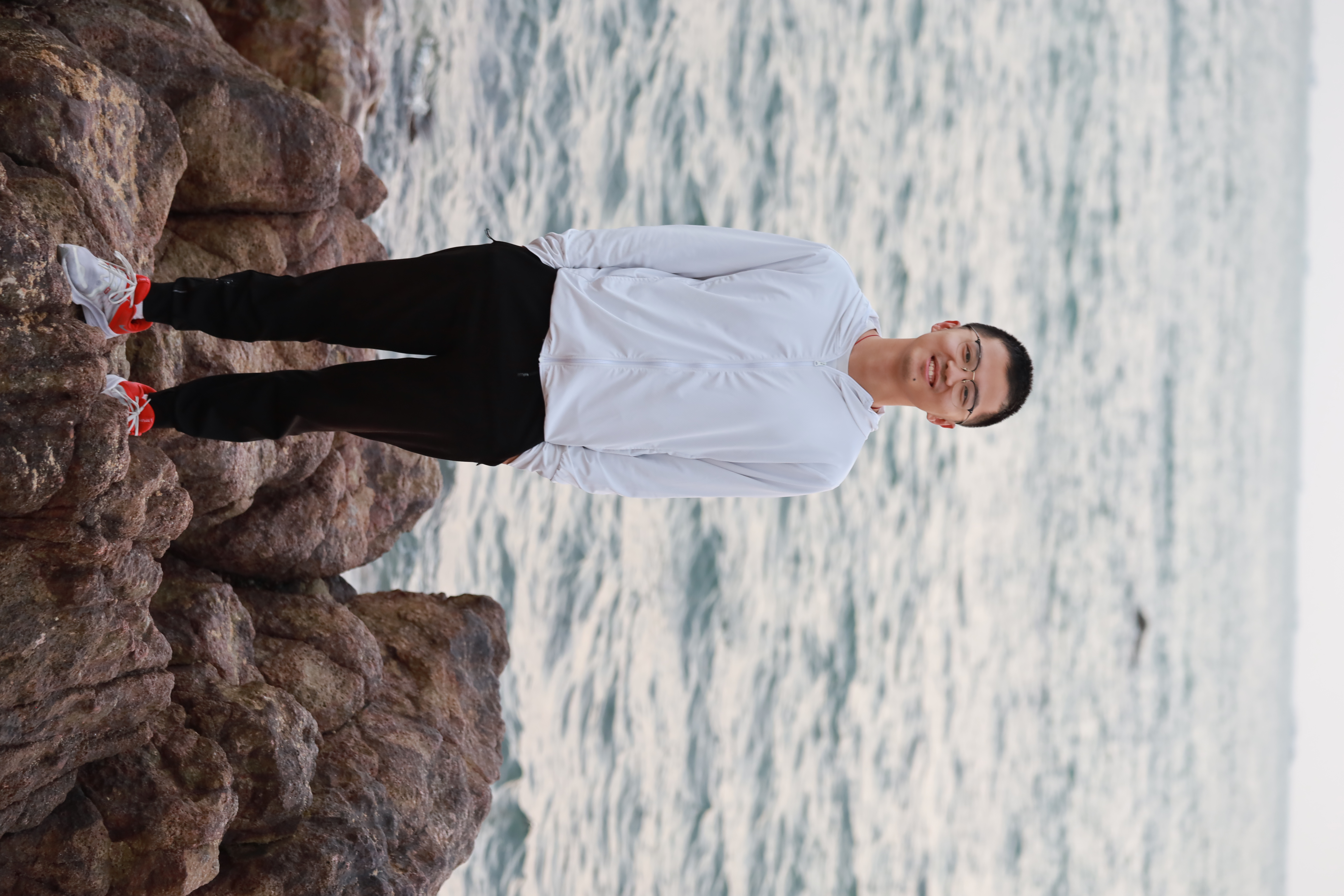 Dong Huang standing on rocks beside the sea